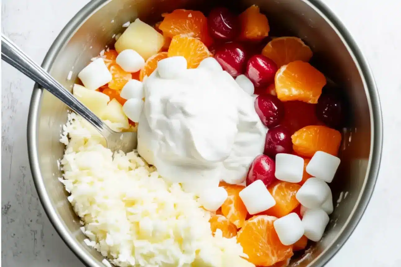 A close-up of Easter Ambrosia Salad with a predominantly white, velvety texture, where the fruits subtly peek through as gentle bursts of color, creating a soft and luscious look.


