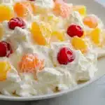 A rustic yet elegant presentation of Ambrosia Salad, where the Cool Whip mixture is the dominant white color, enveloping the fruit with a rich and creamy consistency.