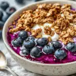 A bowl of creamy Greek yogurt topped with crunchy granola, fresh blueberries, and a drizzle of homemade blueberry syrup.