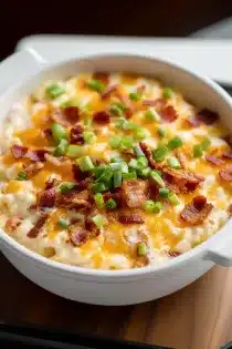A warm, creamy bacon cheddar dip topped with melted cheese, crispy bacon bits, and fresh green onions in a white serving bowl.