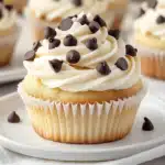 A soft, golden cupcake with whipped vanilla frosting and chocolate chips, displayed on a white plate for a clean and elegant presentation.