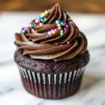 A batch of cupcakes with creamy chocolate frosting and colorful sprinkles, ready for a birthday party spread.