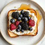 A fresh and vibrant ricotta toast topped with strawberries, blueberries, and a hint of lemon zest for a bright and refreshing flavor.