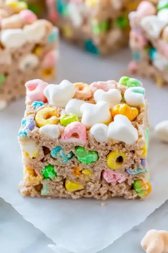 A close-up of a homemade Lucky Charms treat bar, featuring colorful cereal pieces, gooey marshmallow coating, and a drizzle of frosting on top.