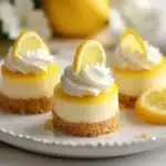 A single mini lemon cheesecake with a bite taken out, revealing the creamy layers of cheesecake and tangy lemon curd, set against a backdrop of fresh lemons and greenery.