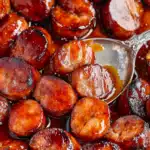 A platter of smoky BBQ sausage bites glazed in a rich barbecue sauce, garnished with fresh parsley and served with toothpicks for easy snacking.