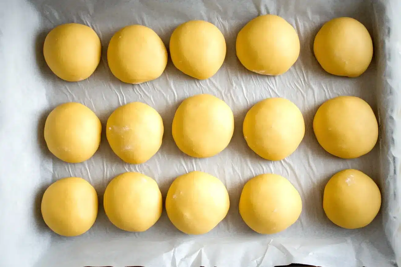 Rows of perfectly shaped donut dough balls on parchment paper before their second rise and frying