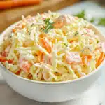 Dairy-free KFC-style coleslaw in a white bowl garnished with dill, showing the perfect texture of finely chopped cabbage and carrots in a creamy mayo and vinegar dressing.