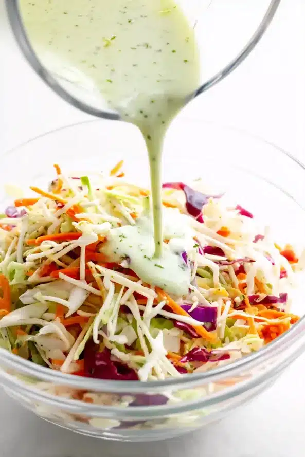 Creamy light green cilantro lime dressing being poured from above onto a bowl of colorful shredded cabbage mix.