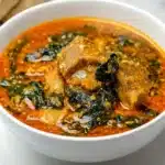 A bowl of Nigerian Egusi soup with a blend of meats, ground melon seeds, spinach, and palm oil in a delicious broth.