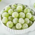 Green grapes rolled in sugar and frozen, served in a bowl for a sweet, refreshing treat.