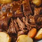 Braised chuck roast in rich gravy with halved baby potatoes and carrots, cooked to perfection in a Dutch oven.