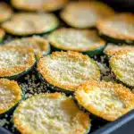 Close-up of golden, crispy zucchini chips arranged neatly on a parchment-lined baking sheet