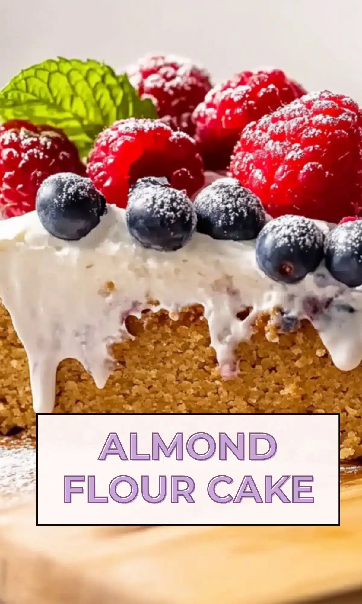 Close-up of powdered sugar-dusted raspberries and blueberries with bright green mint leaves atop white coconut cream on an almond flour cake