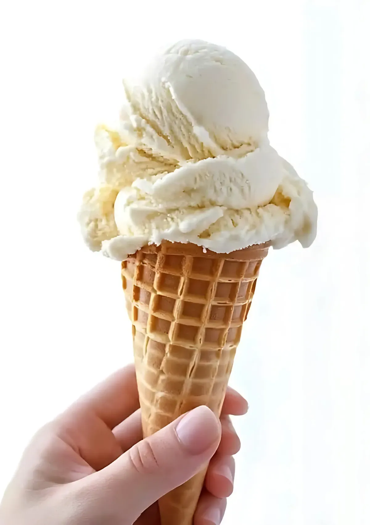 Hand holding a waffle cone with three scoops of creamy vanilla ice cream