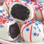 Close view of patriotic Oreo truffles with white coating, red and blue drizzle, and star-shaped sprinkles on a white plate