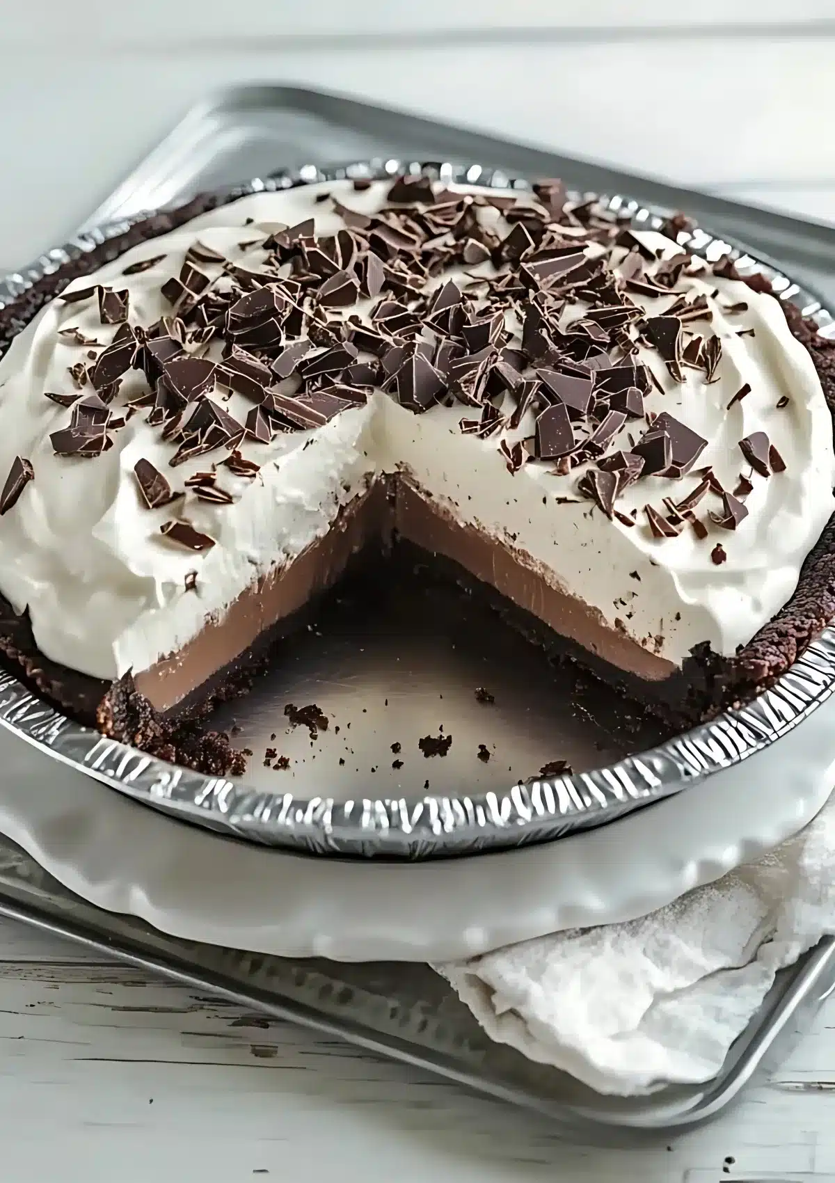No-bake chocolate pie in aluminum pan with a slice removed showing creamy chocolate filling and whipped topping with chocolate shavings