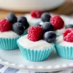Vegan frozen yogurt cups in teal liners topped with blueberries and raspberries on a white plate, with a coral banner at the bottom reading 'EASY FROZEN YOGURT BITES (VEGAN)' and the website URL oliviahealthyliving.com."