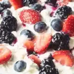 Close-up macro shot of triple berry cheesecake fruit salad showing texture details of creamy white filling with fresh red, blue and black berries