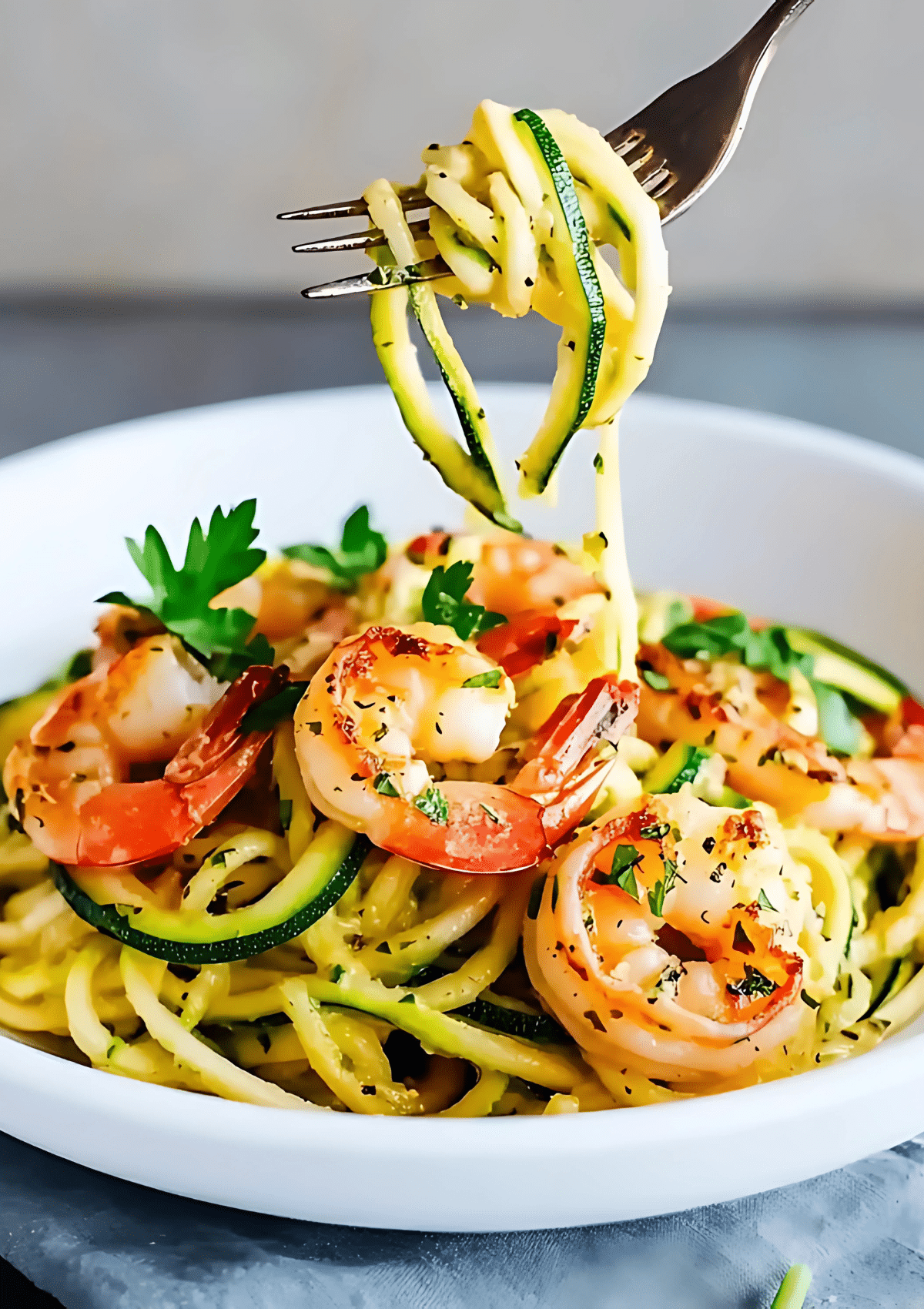 Fork twirling zucchini noodles with shrimp scampi in white bowl, showing spiralized zucchini wrapped around fork with cooked pink shrimp