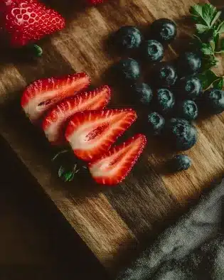 Fresh strawberry slices and whole blueberries arranged on rustic wooden cutting board