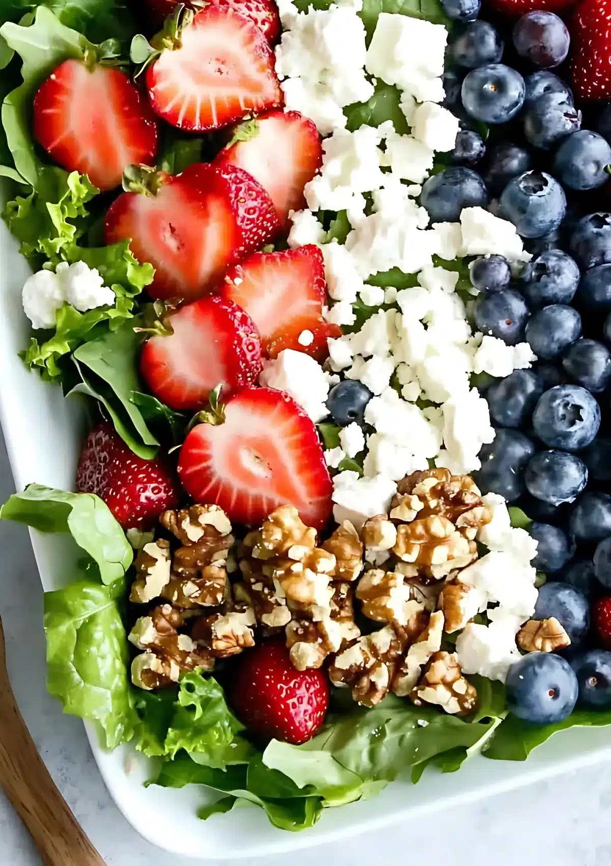 Close-up view of Red White and Blue Salad on a white plate showing the colorful arrangement of strawberries, feta cheese, blueberries and glazed walnuts