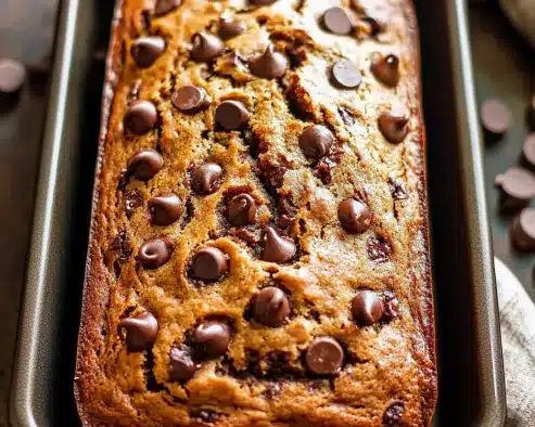 Golden brown chocolate chip banana bread baked in metal loaf pan with abundant chocolate chips scattered across the caramelized surface