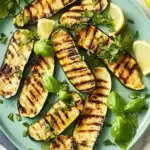 Close-up of tender-crisp grilled zucchini slices garnished with fresh basil leaves on a turquoise plate with a fork, ready to serve