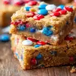 Close-up of two Fireworks Blondies stacked on a wooden surface, showcasing the golden brown caramelized texture with colorful red, white, and blue M&Ms throughout and on top