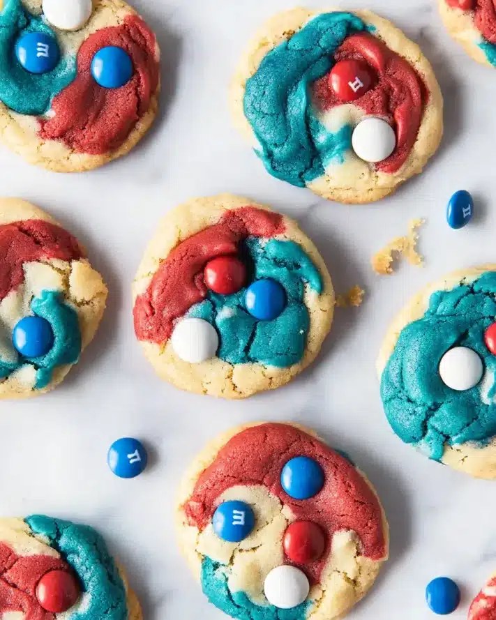 Overhead view of soft-baked red, white and blue cookies with M&Ms scattered on a white marble surface