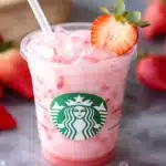 Starbucks Pink Drink in clear cup with fresh strawberries in the background on a marble surface