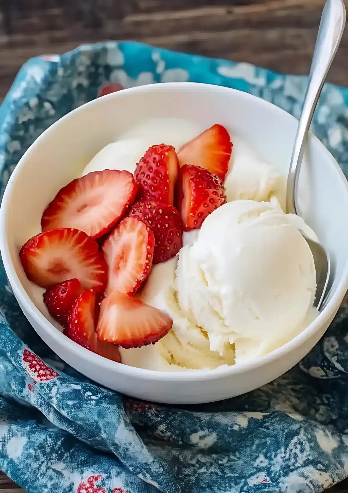 Close-up of vanilla ice cream with sliced strawberries in a white bowl on a blue patterned cloth