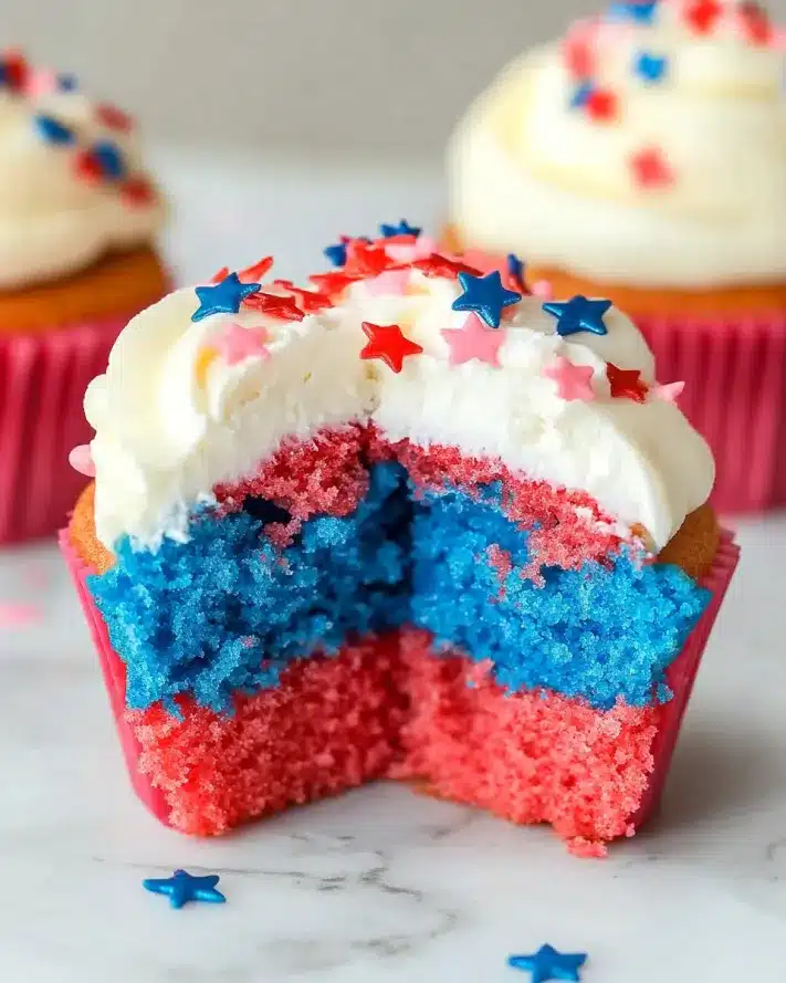 Close-up of a star-sprinkled red white and blue cupcake with a bite taken showing the vibrant interior layers