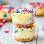 Muffin tin filled with vanilla cupcakes topped with white frosting and red and blue sprinkles in a Fourth of July theme