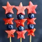 Square image of three patriotic fruit kabobs featuring star-shaped watermelon pieces and plump blueberries arranged in an eye-catching pattern for Memorial Day or Fourth of July gatherings
