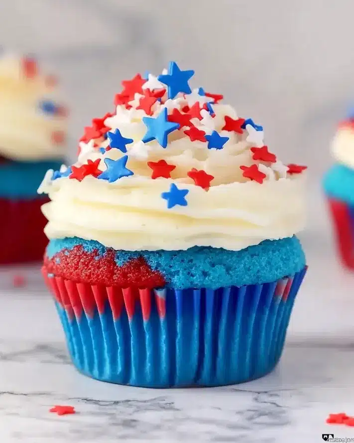 Close-up of a red white and blue cupcake showing the cross-section of colorful cake layers and star-topped frosting