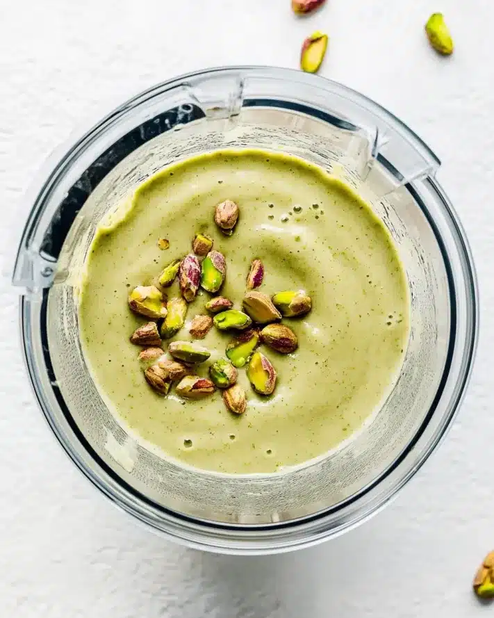 Overhead shot of a blender filled with thick pistachio smoothie, topped with whole shelled pistachios.