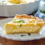 Single slice of quiche with rice crust on white scalloped plate showing layered custard filling and golden top