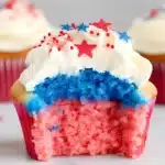 Close-up of a patriotic red white and blue cupcake with a bite taken out showing layered colors and star sprinkles