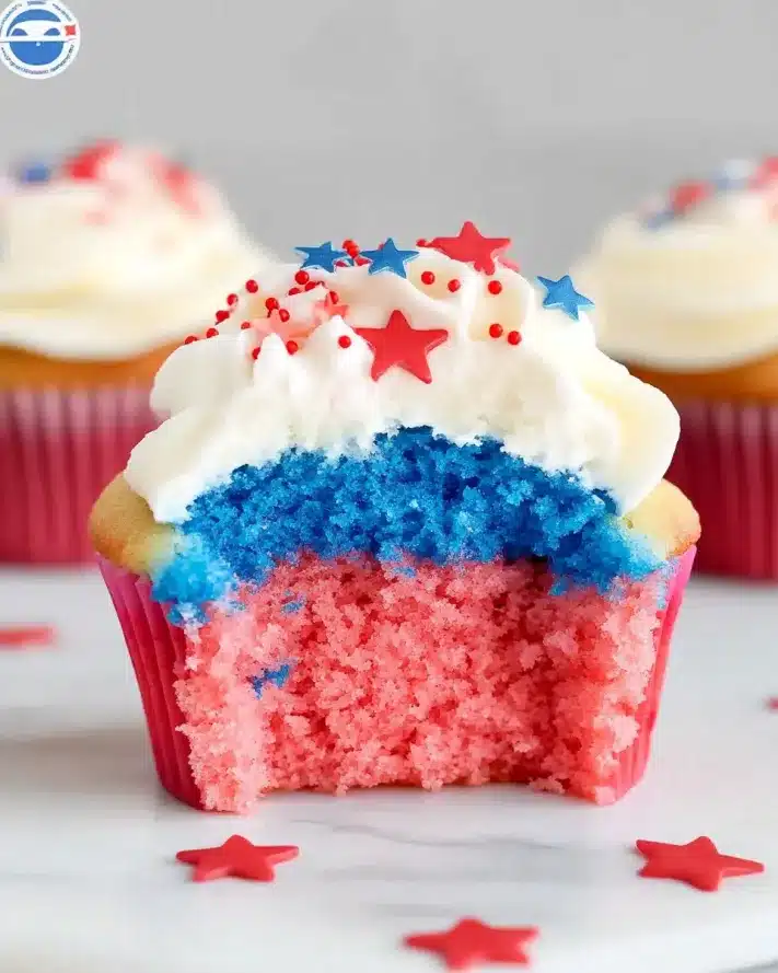 Red, white and blue striped cupcake with a red cake base, blue liner, and white frosting swirl on a marble surface