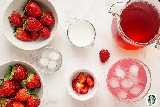 Top-down view of Starbucks Pink Drink ingredients including fresh strawberries, coconut milk, passion tea, ice cubes, and sliced strawberries on a white textured background