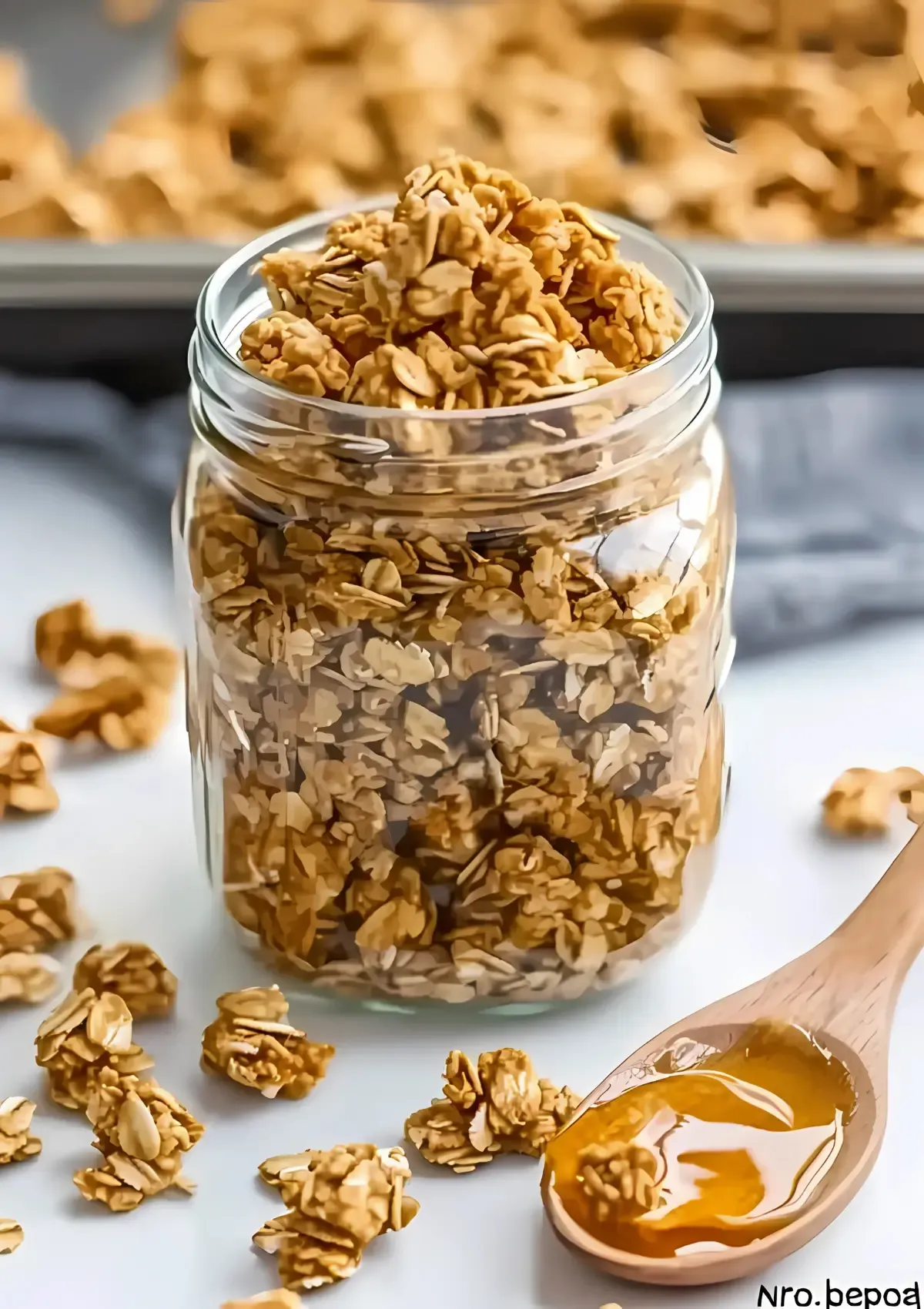 Mason jar packed with golden peanut butter granola clusters, wooden spoon with honey drizzle, scattered granola pieces on white marble surface
