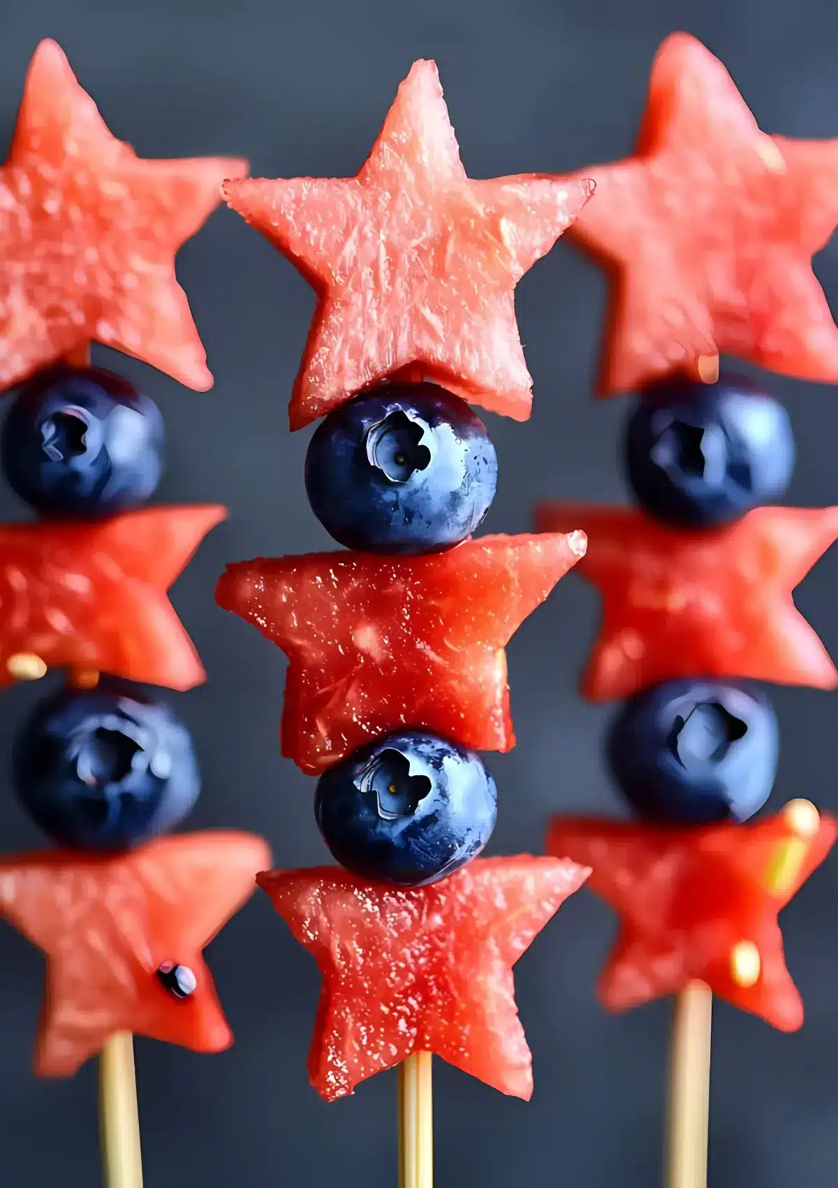 Detailed close-up of a patriotic fruit kabob showing juicy watermelon stars alternating with fresh blueberries on a wooden skewer against a dark background