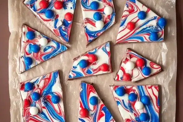 Patriotic chocolate bark cut into triangular pieces on parchment paper, featuring red white blue swirled pattern with candy ball decorations