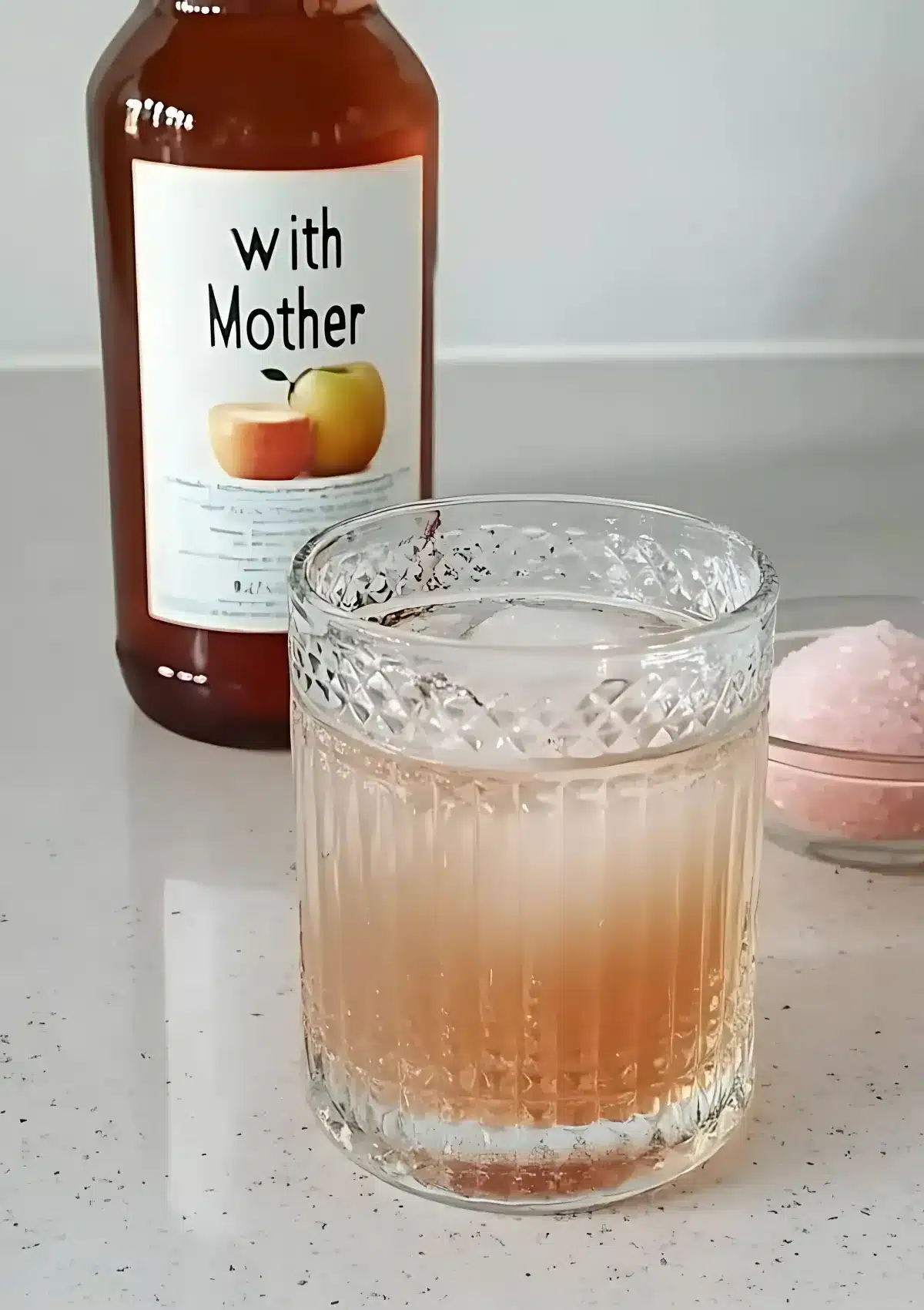Clear vintage glass filled with apple cider vinegar and pink salt drink, placed in front of a labeled bottle with “with Mother” text, perfect for daily detox and gut health.