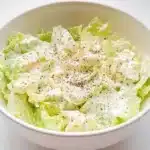 Final presentation of Swedish pizza salad in white bowl showing creamy dressed lettuce with black pepper seasoning