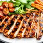Sliced ​​BBQ chicken breast served on white plate with fresh cherry tomatoes and carrot sticks