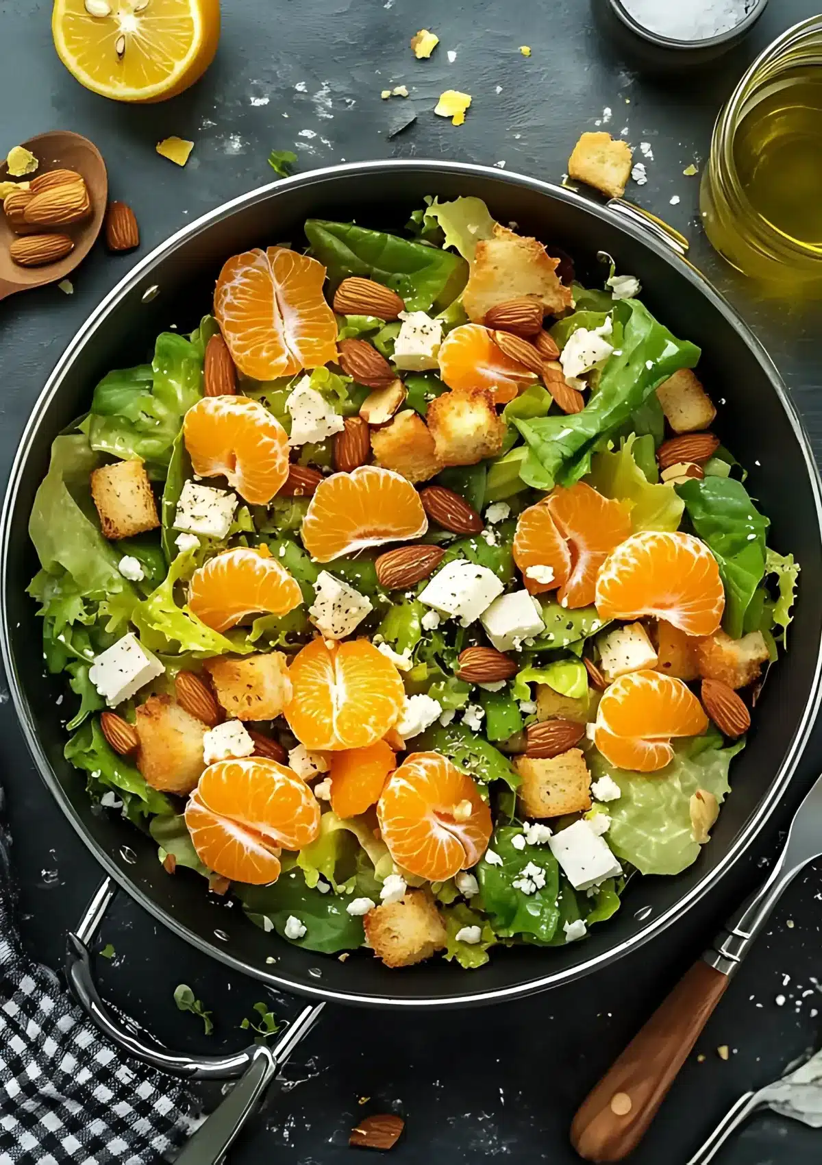 Overhead shot of mandarin orange salad in black pan with whole almonds, olive oil and lemon visible around the pan