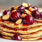 Stack of pancakes topped with cherry almond topping recipe featuring glossy cherries and sliced ​​almonds