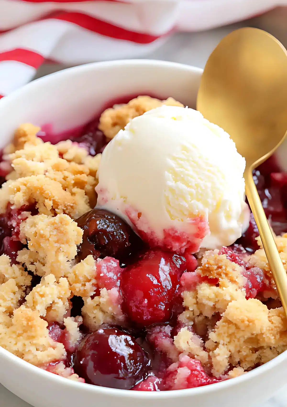Serving of cherry cobbler with vanilla ice cream showing golden topping and juicy cherries